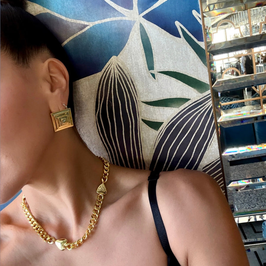 Person wearing gold jewelry with a blue and white patterned rug in the background