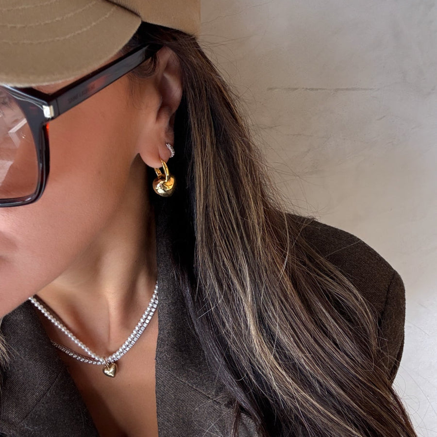 Close-up of a person wearing gold earrings, sunglasses, and a beige cap.
