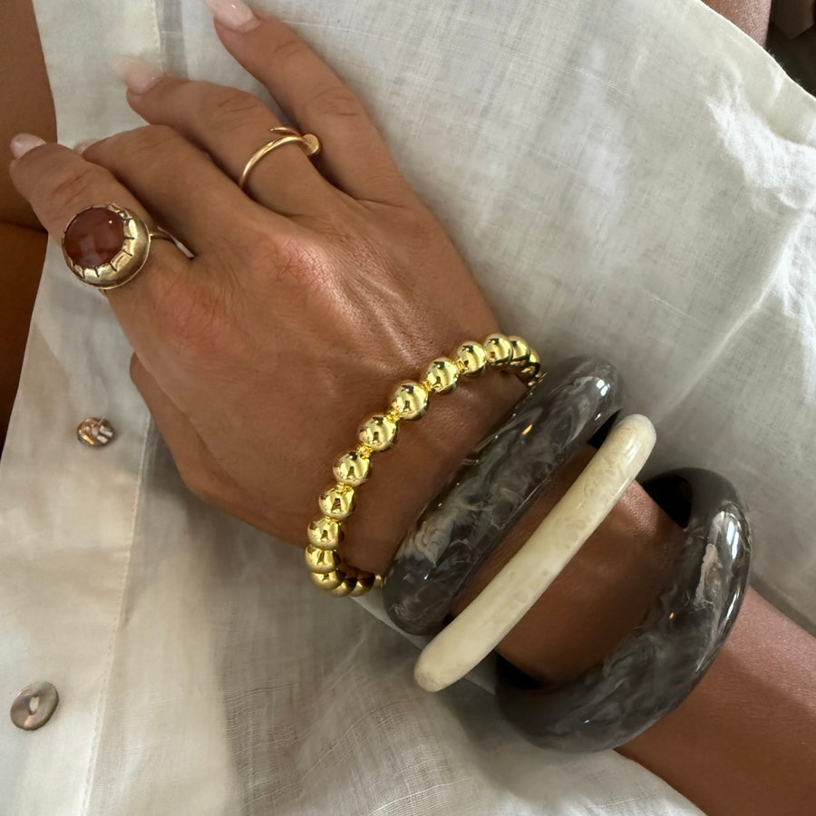 Hand wearing gold bracelet, ring, and gray bangles on a light fabric background